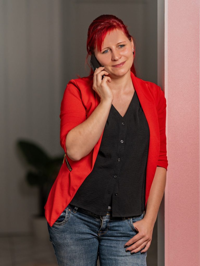 Frau mit rotem Blazer und schwarzem Oberteil, die am Telefon lächelt.