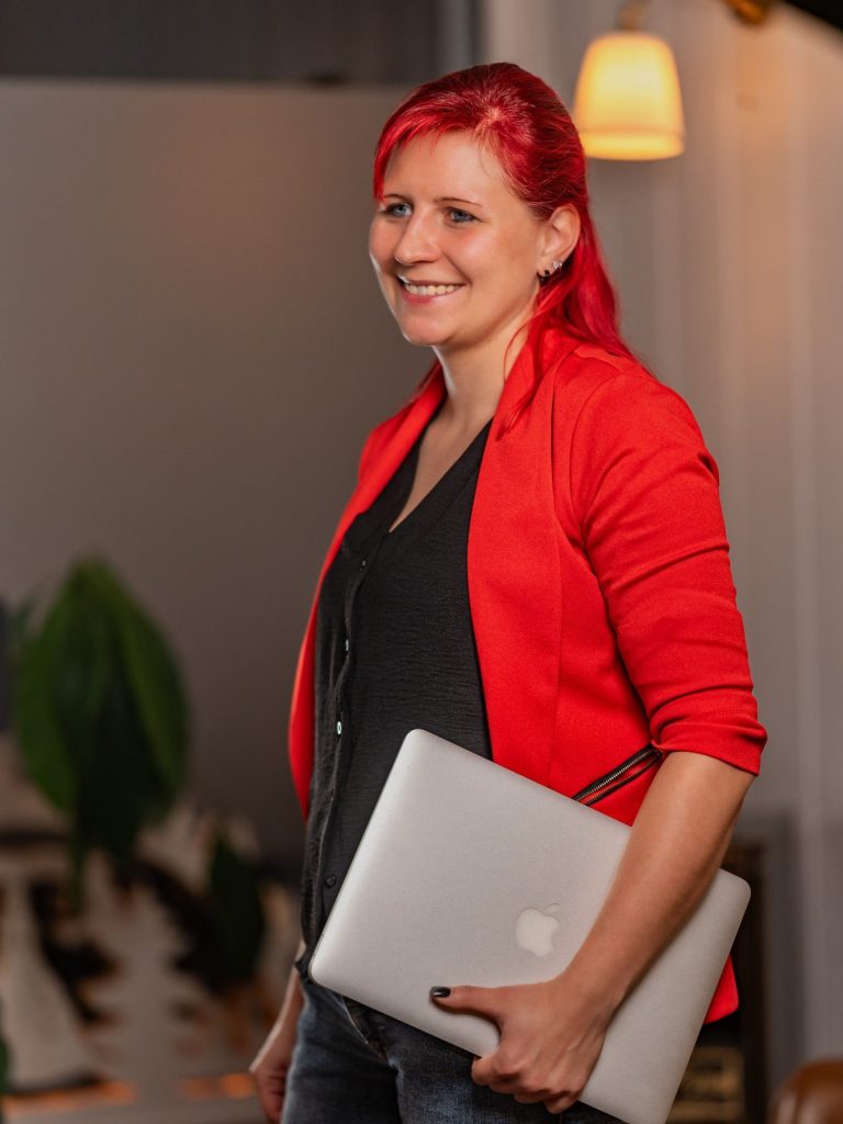 Frau mit rotem Blazer und schwarzem Oberteil, die am Telefon lächelt.