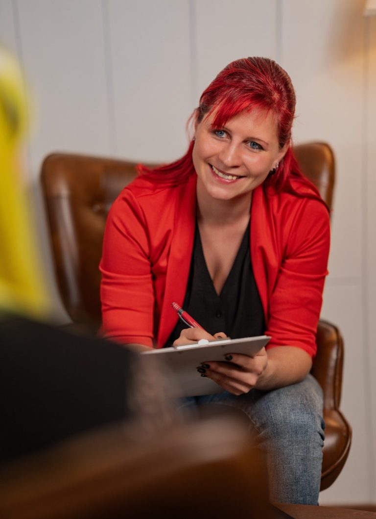 Eine Hand mit pinkem Stift schreibt auf ein Arbeitsblatt mit Diagramm und Text.